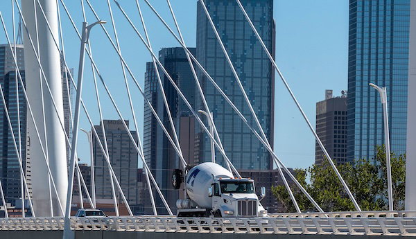 A white truck driving across a cable-stayed bridge with a city skyline in the background.