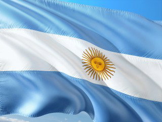 The Argentine flag waving in the wind, with light blue and white stripes and a sun emblem in the center.
