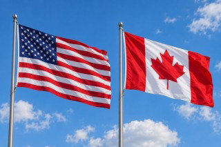 The United States and Canadian flags flying on poles against a blue sky.