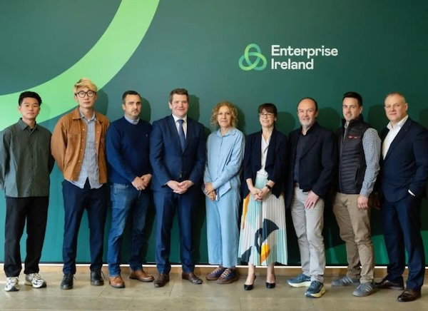 Nine people standing in a row in front of a green wall with an Enterprise Ireland logo.