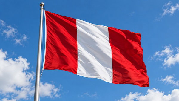 A red and white Peruvian flag waving on a pole against a blue sky.