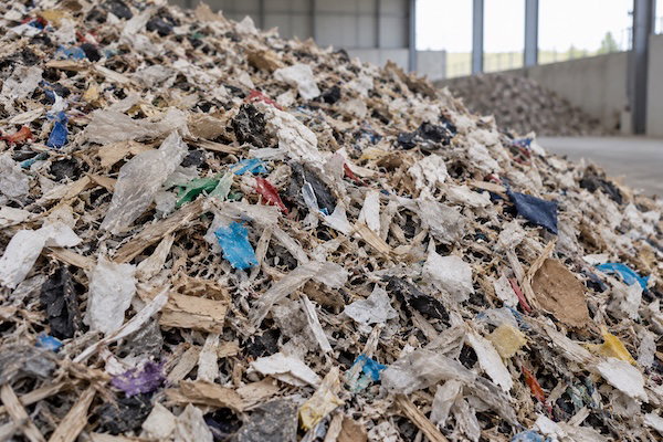 A large pile of shredded mixed waste sits inside an industrial building.